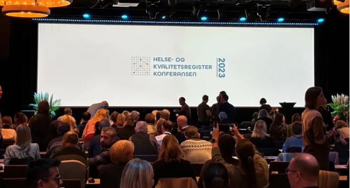 En gruppe mennesker som sitter i et rom med en stor skjerm
