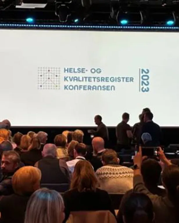 En gruppe mennesker som sitter i et rom med en stor skjerm