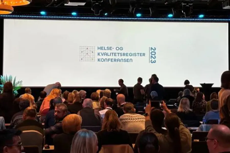 En gruppe mennesker som sitter i et rom med en stor skjerm