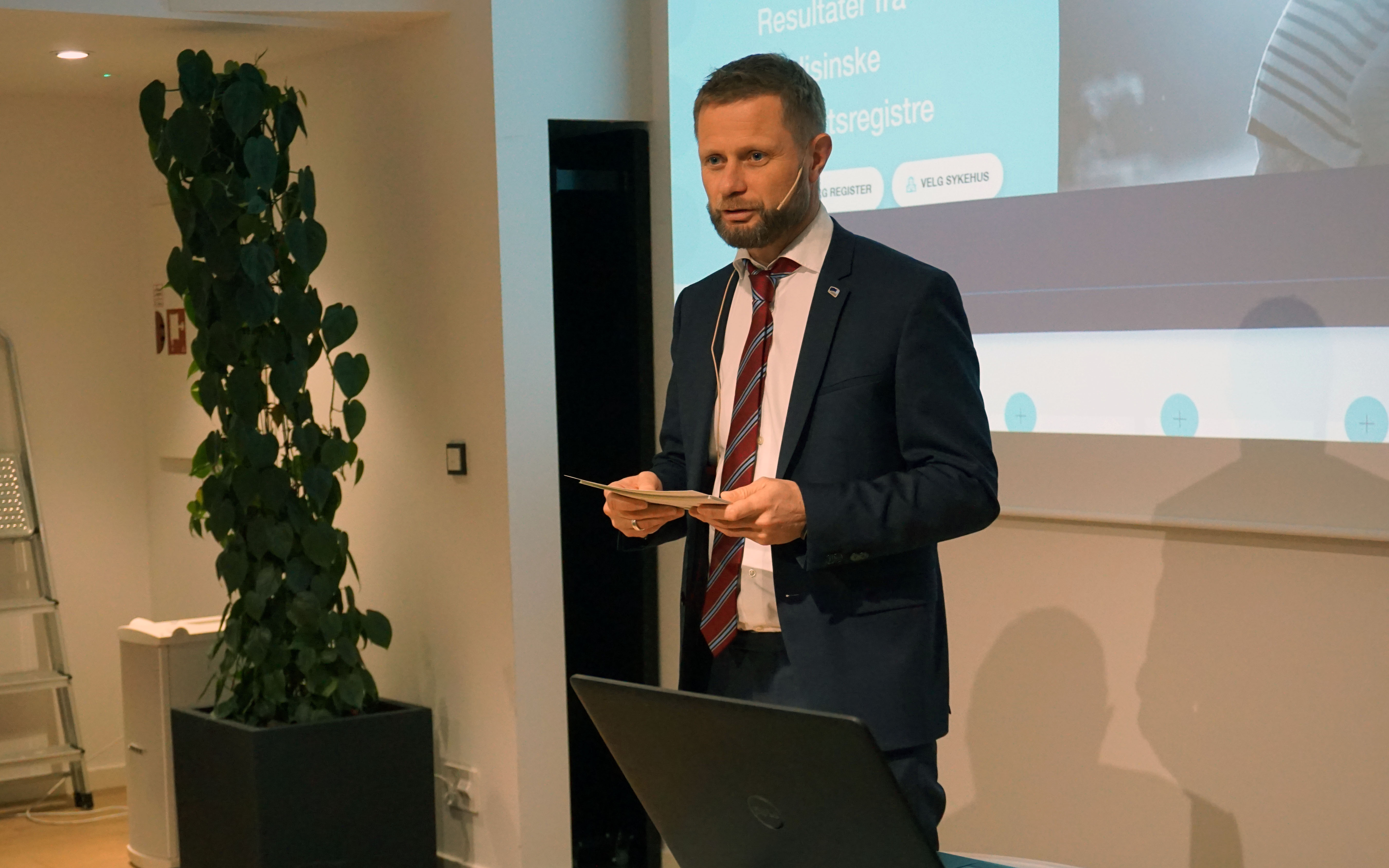 A man in a suit holding a book in front of a projector screen
