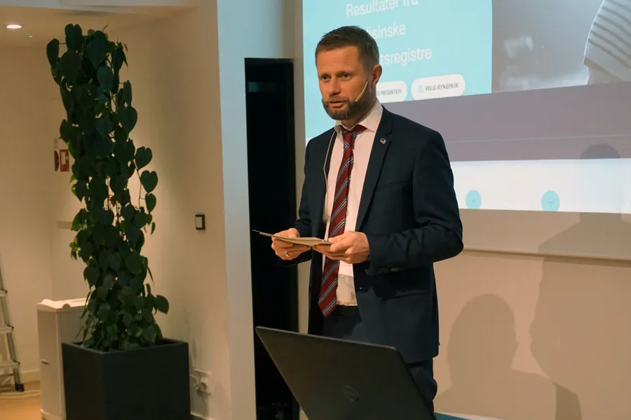 A man in a suit holding a book in front of a projector screen