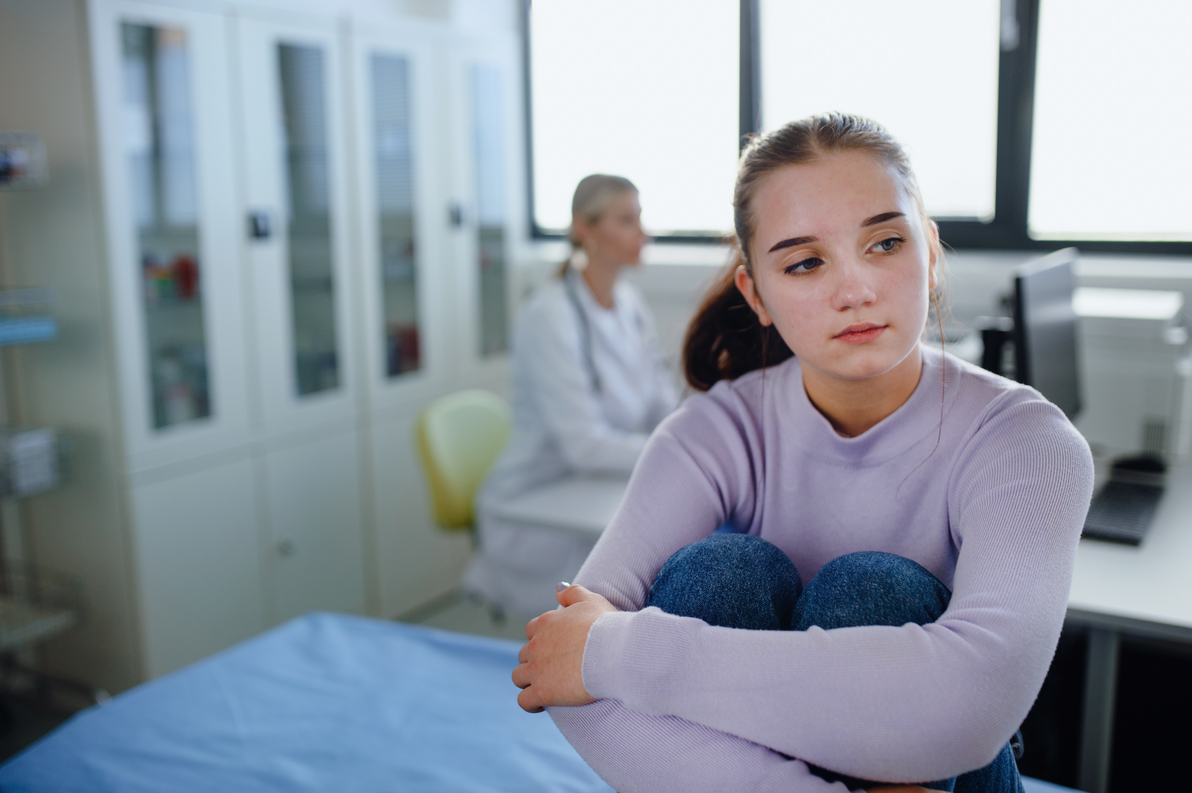 Young girl sitting in an examination room with a doctor in the background